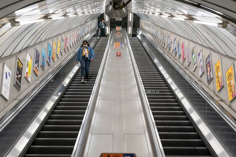 A woman walks down an empty escalator on the London Underground.