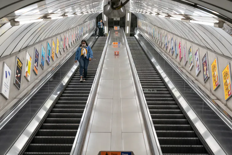 A woman walks down an empty escalator on the London Underground.