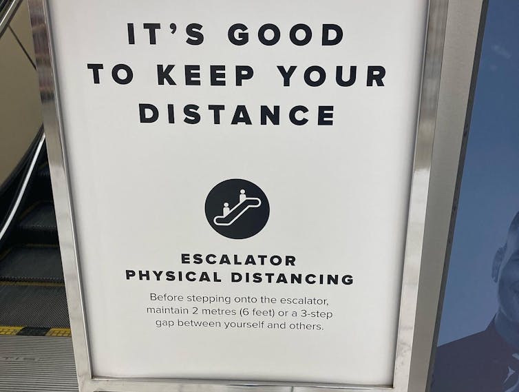 Sign at an escalator says 'it's good to keep your distance....Maintain 2 metres / 6 feet or a 3 step gap between you and others.'