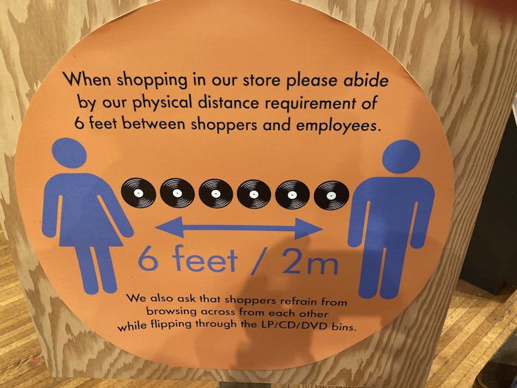 Store signage shows a line of six LP records and distancing arrows marking 2 metres or six feet.
