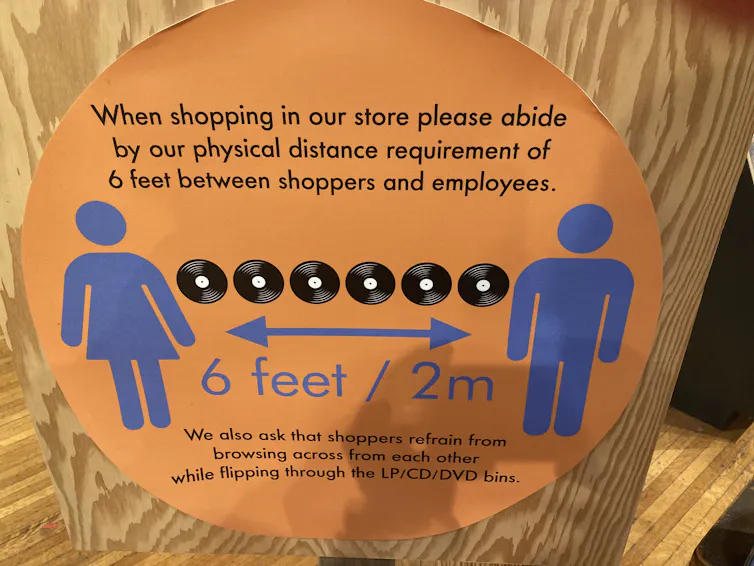 Store signage shows a line of six LP records and distancing arrows marking 2 metres or six feet.