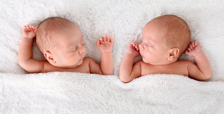 Newborn twins sleep with raised arms.