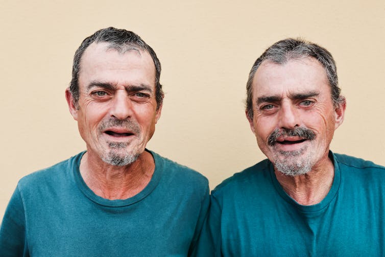 Older men stand beside each other, smiling.