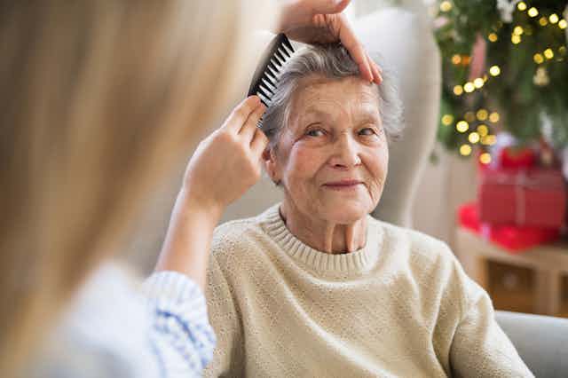 Carer combing elderly woman's hair at home in front of Christmas tree