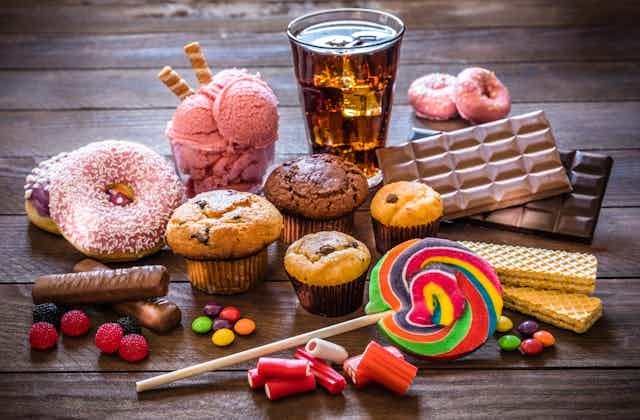 A sampling of sugary sweets, including donuts, muffins, cookies, chocolate, a lollipop and a soft drink.