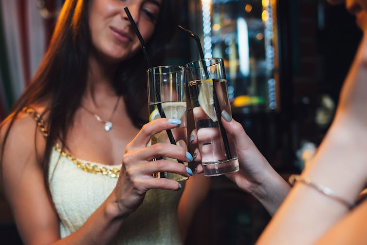 Two people cheersing glasses of water with lemon