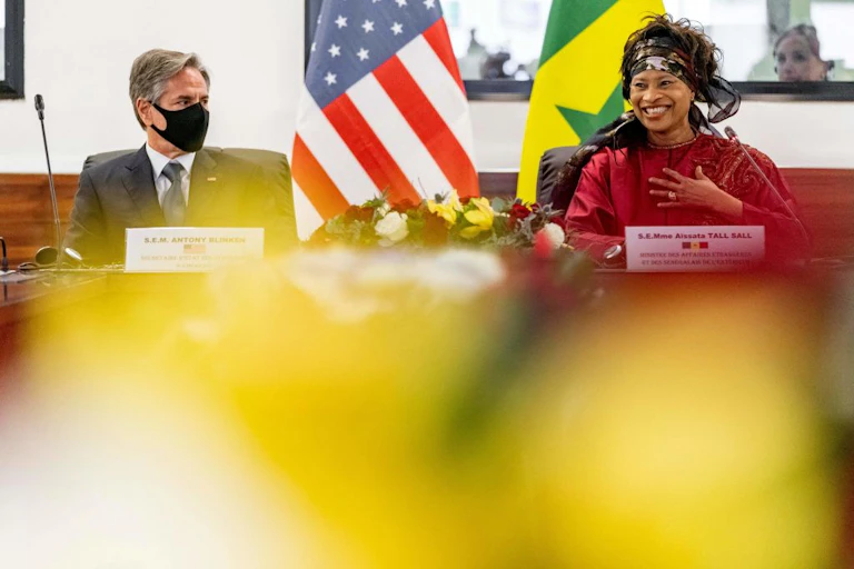 Man with a mask looking at a smiling women with US and Senegalese flags in the background