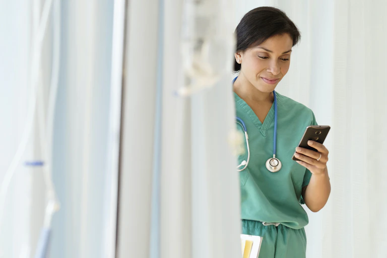 woman in scrubs smiles looking at smartphone