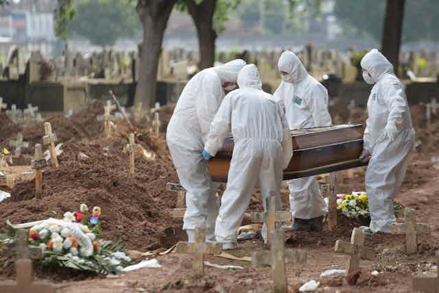 People in Brazil in PPE carrying a coffin to a grave