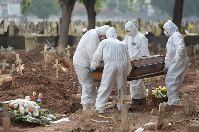 People in Brazil in PPE carrying a coffin to a grave