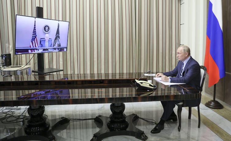 Russian president, Vladimir Putin, sits at a table in front of the Russian flag talking with US president Joe Biden via video link.