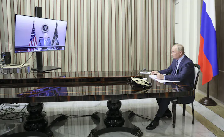 Russian president, Vladimir Putin, sits at a table in front of the Russian flag talking with US president Joe Biden via video link.
