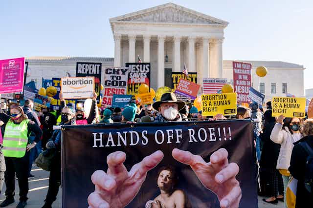 A man holds a sign that reads 'Hands Off Roe!!!' amid a crowd of protesters with the U.S. Supreme Court building behind them.