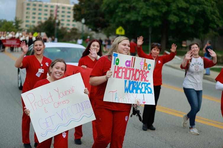 Women in red scrubs hold signs encouraging people to get vaccinated