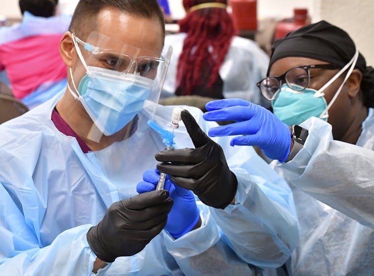 Two people wearing face masks and scrubs fill a syringe
