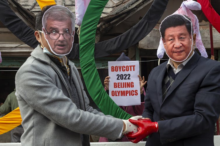 Two people wear masks with a sign reading 'boycott 2022 olympics'