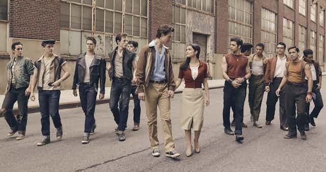 A young couple walks down a city street surrounded by young men.