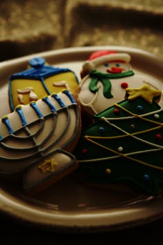 Cookies shaped like a menorah, a dreidel, a snowman, and a Christmas tree sit on a plate.