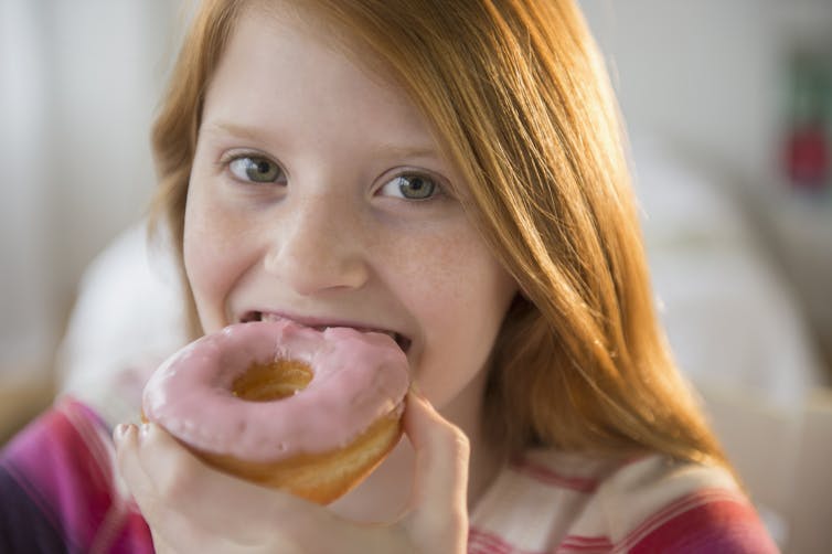 A young girl eats a pink-glazed donut.