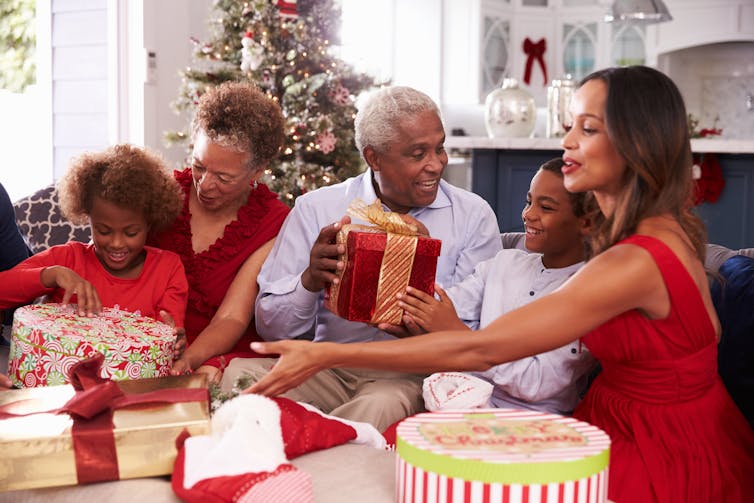 A family looks at wrapped gifts in front of a Christmas tree