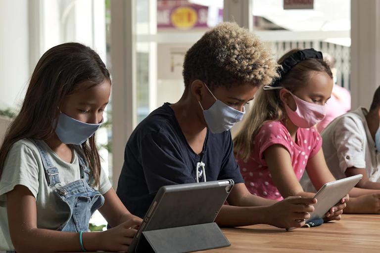 Students seen with devices at a table wearing masks.