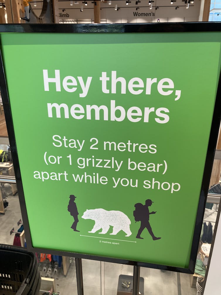 Sign shows a bear with disancing arrows and says stay two metres or one grizzly bear apart.