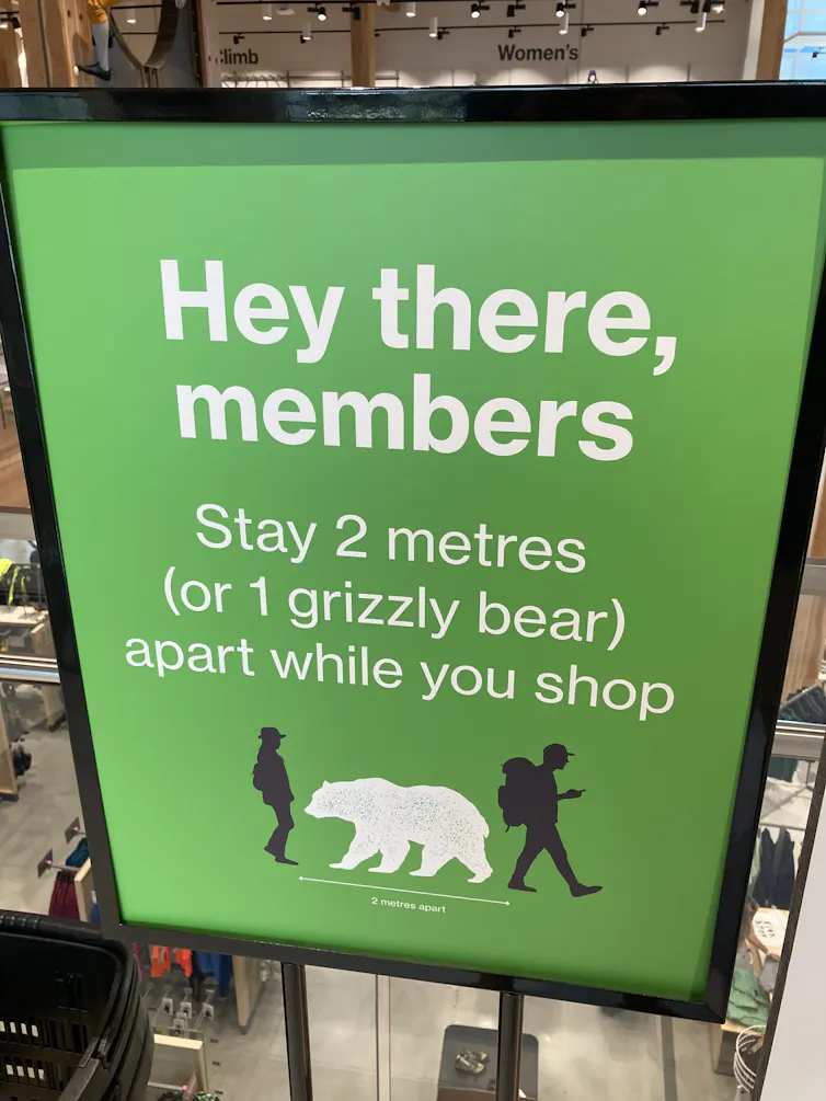 Sign shows a bear with disancing arrows and says stay two metres or one grizzly bear apart.