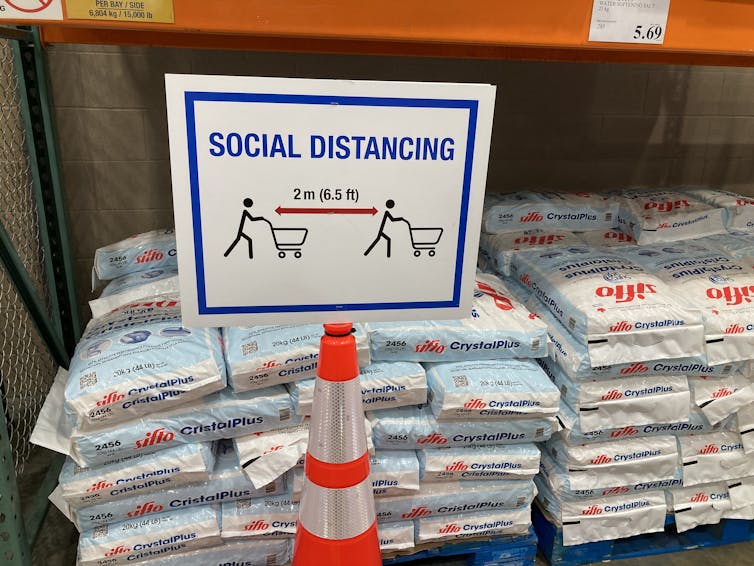 Sign showing distancing arrows and a shopping cart that says social distancing 2 metres or 6.5 feet apart.