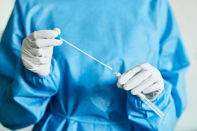 Un profesional médico en ropa quirúrgica sostiene un hisopo con un cilindro pequeño.