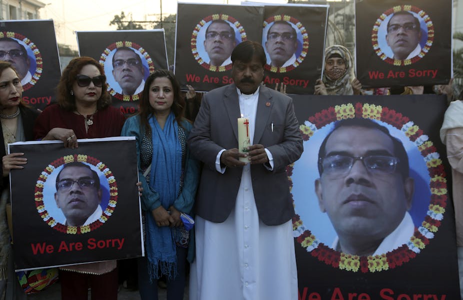 A man dressed in a jacket and white long shirt holding a candle, while two women standing next to home hold the photograph of a man, who was lynched in Pakistan.