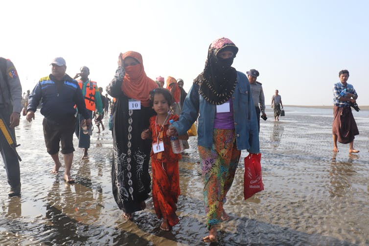 Several men and women, with faces covered, walk on a beach after being arrested.