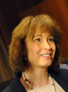 Judge Millett at her confirmation hearing, wearing pearls, a beige shirt and dark jacket. She has short, brown hair.