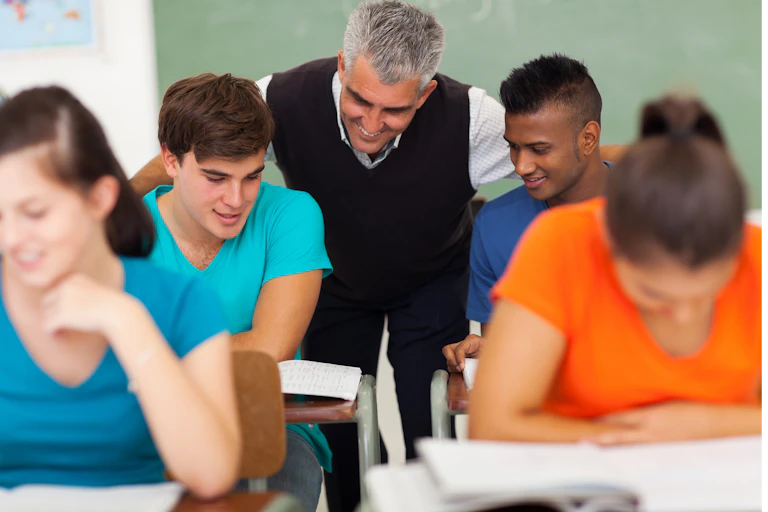 Male teacher encouraging two boys in class with two girls sitting in front of them