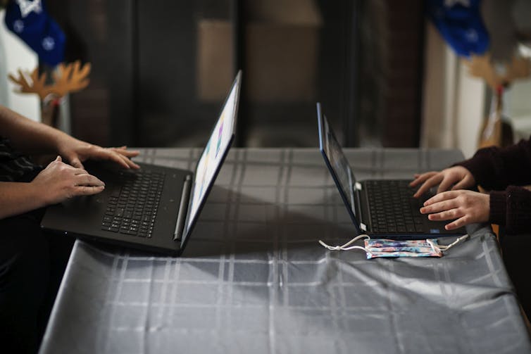 A mother and daughter, with only their hands visible, work on two laptops at a table