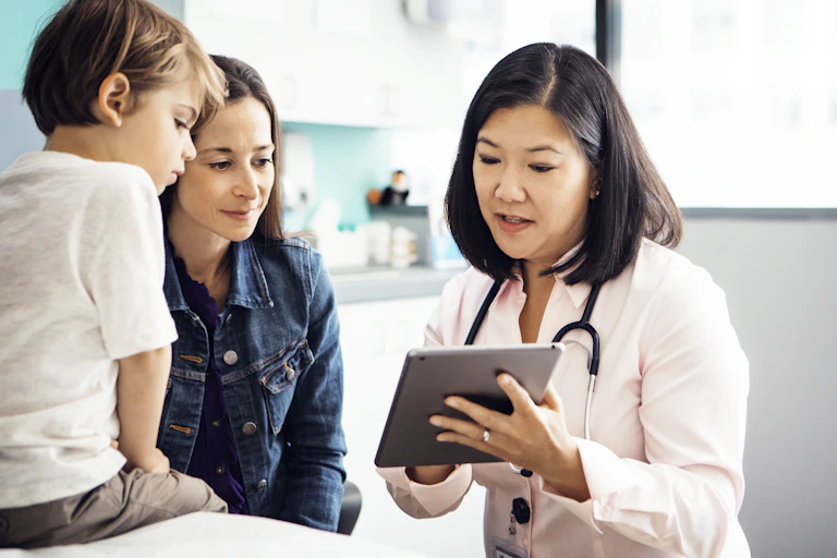 Doctor explaining report on tablet computer to mother and young child in clinic.