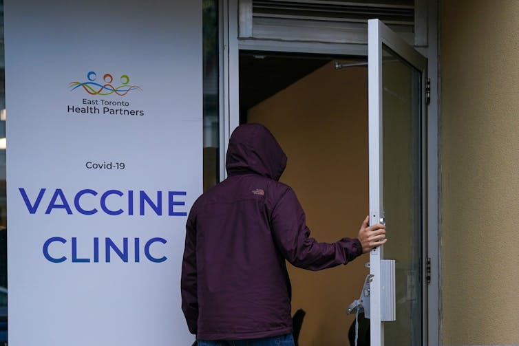 A person in a hooded coat seen from behind entering a COVID-19 vaccine clinic