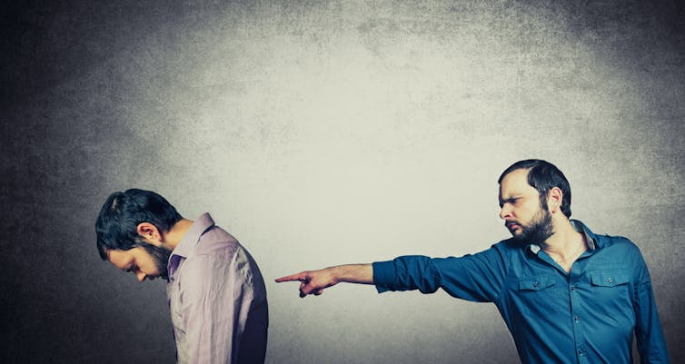 Man pointing finger, shaming other man, whose head is hung low