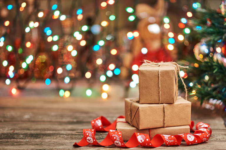 A stack of three gifts wrapped in brown paper, with a tree and twinkling lights in the background