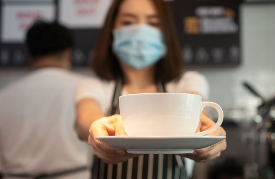 Woman wearing face mask serves cup of coffee.