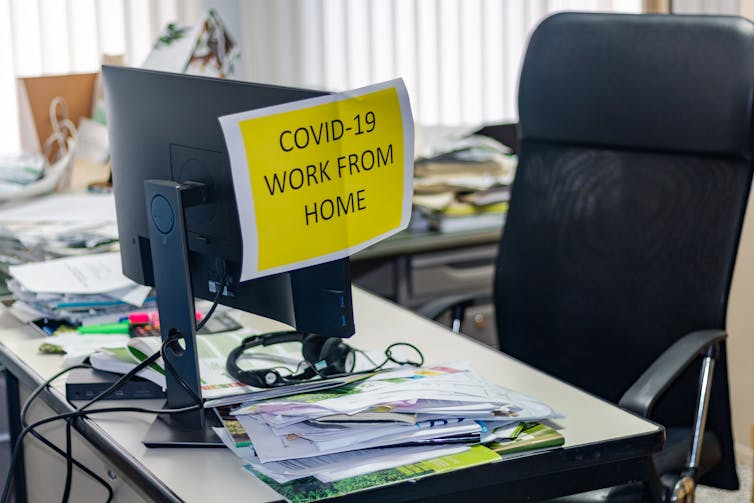 Unoccupied office desk with sign showing instructions to work from home.