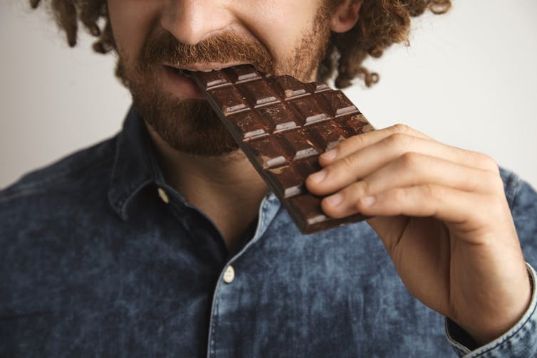 Close up of a man biting into a large bar of chocolate.