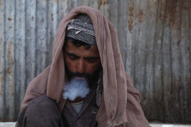 An Afghan man in traditional clothes smoking heroin in Jalalabad , Afghanistan.