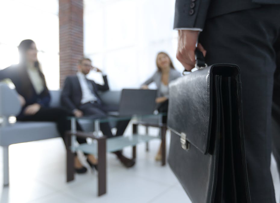 People seen in a meeting room where someone is entering holding a briefcase.