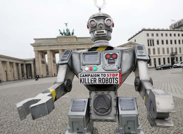 A mockup of a humanoid robot with a bumper sticker on its chest stands in front of the Brandenburg Gate in Germany