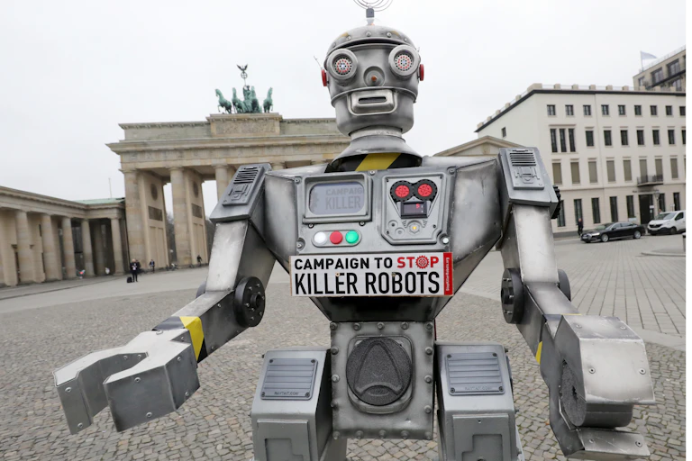 A mockup of a humanoid robot with a bumper sticker on its chest stands in front of the Brandenburg Gate in Germany