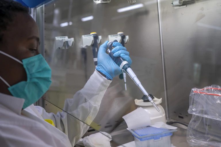 A person wearing a facemask, lab coat and rubber gloves holds a long syringe-like device