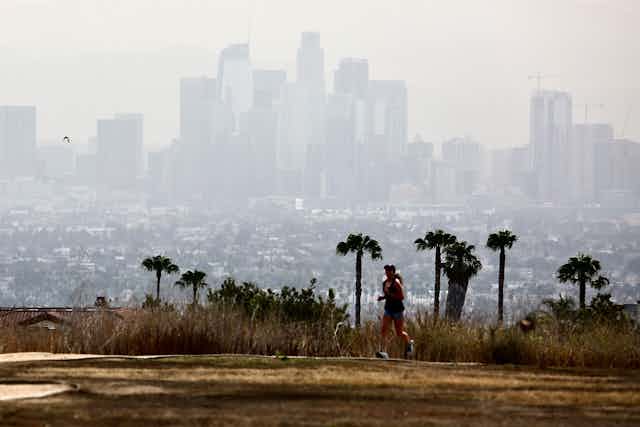 Jogger in an empty park against a smoggy city skyline