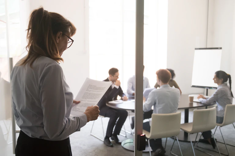 A woman stands at a door looking nervous while a group of peole talk.
