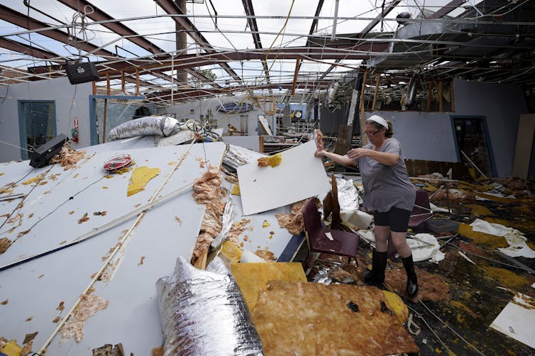 Woman sorts through soggy materials in roofless building