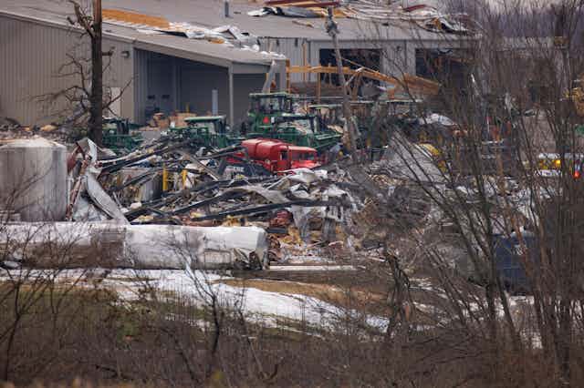 Vehicles covered with debris outside a damaged warehouse